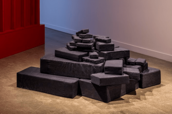 A soft sculpture of variously sized "brick" pillows upholstered in prison-issue denim by Mary Walling Blackburn titled Fort Dun Dun.